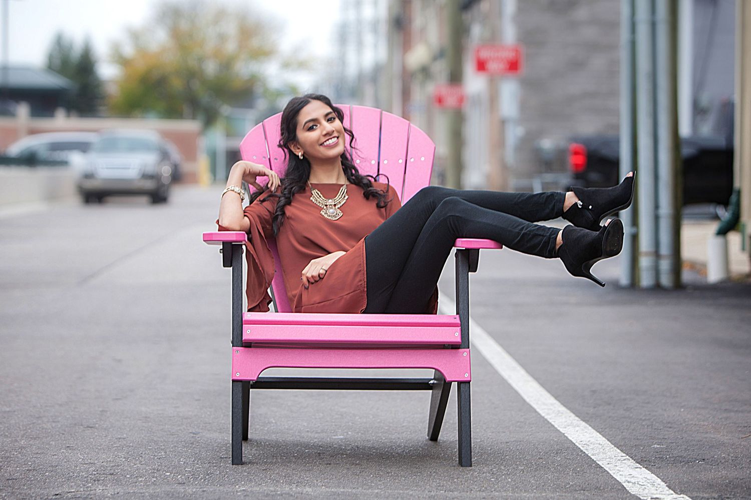 Senior girl portrait in oversized pink chair on urban street,by Jocelyn M. Photography in Rochester, MI