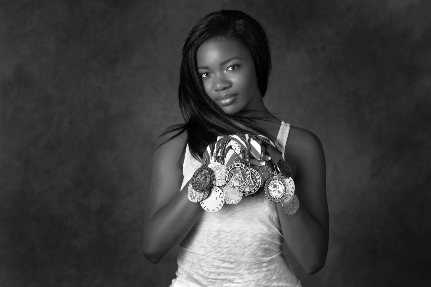 Young Black woman holding multiple medals posing for black and white senior portrait photo.