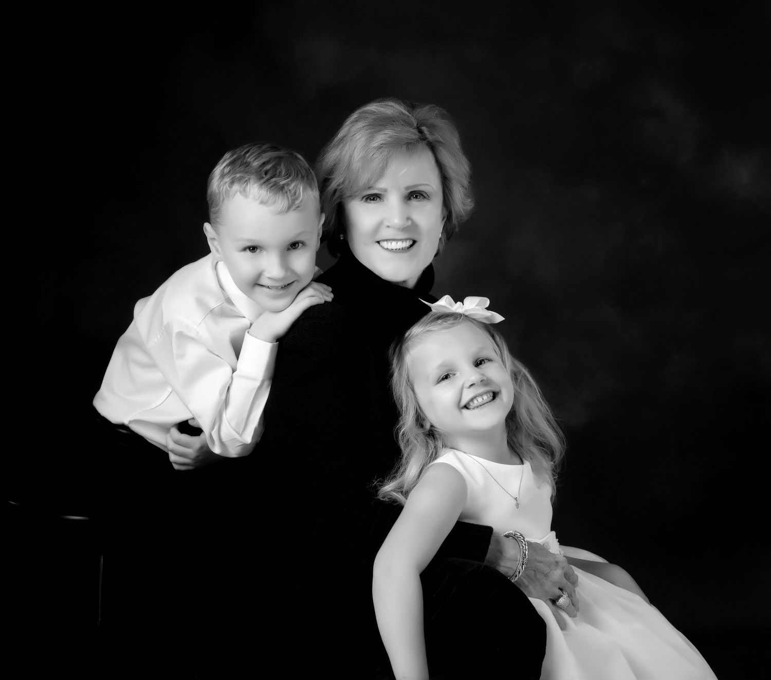 Black and white portrait of a smiling woman with two young children, a boy and girl, in formal attire.