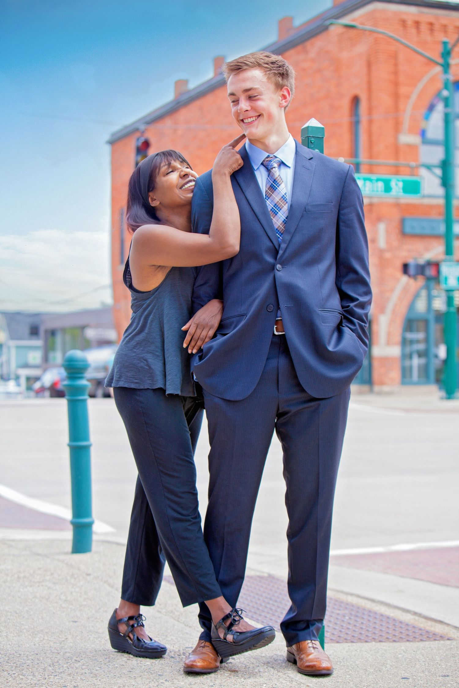 Interracial couple posing outdoors on city street, woman touching mans face affectionately.