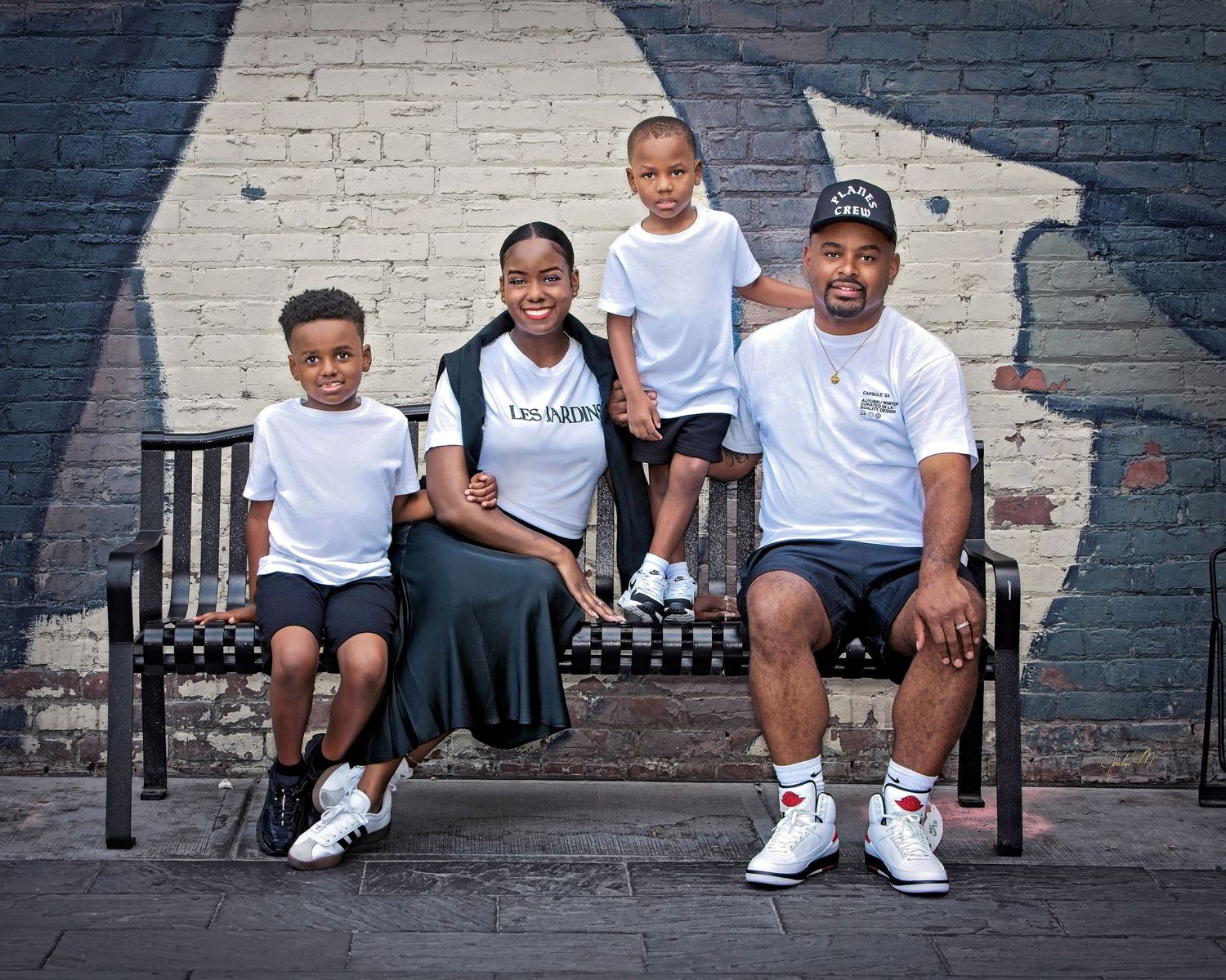 Happy African American family of four posing on a bench in front of a colorful mural wall.