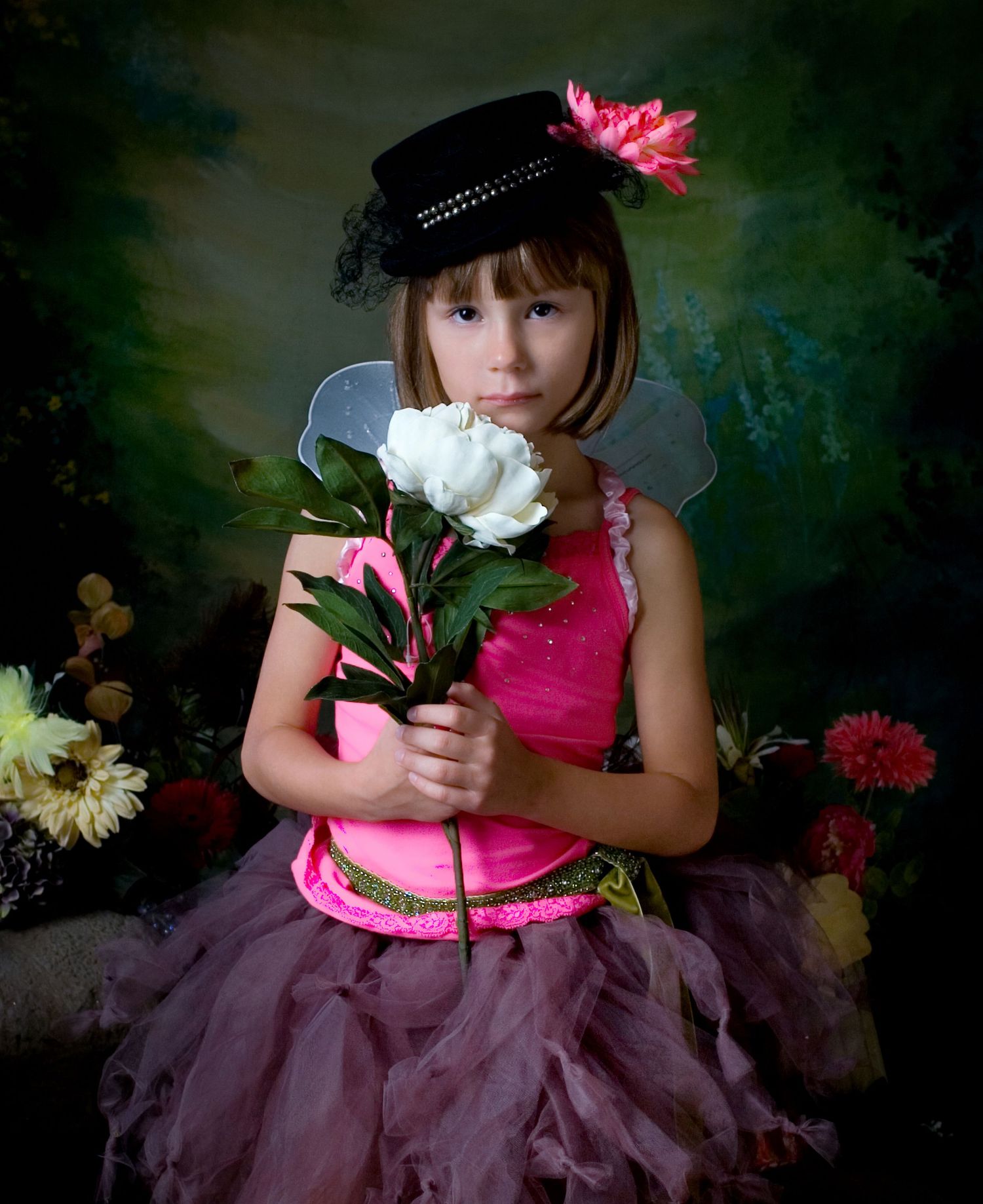 Young girl in fairy costume with black hat, pink top, tutu skirt, holding a white peony flower.