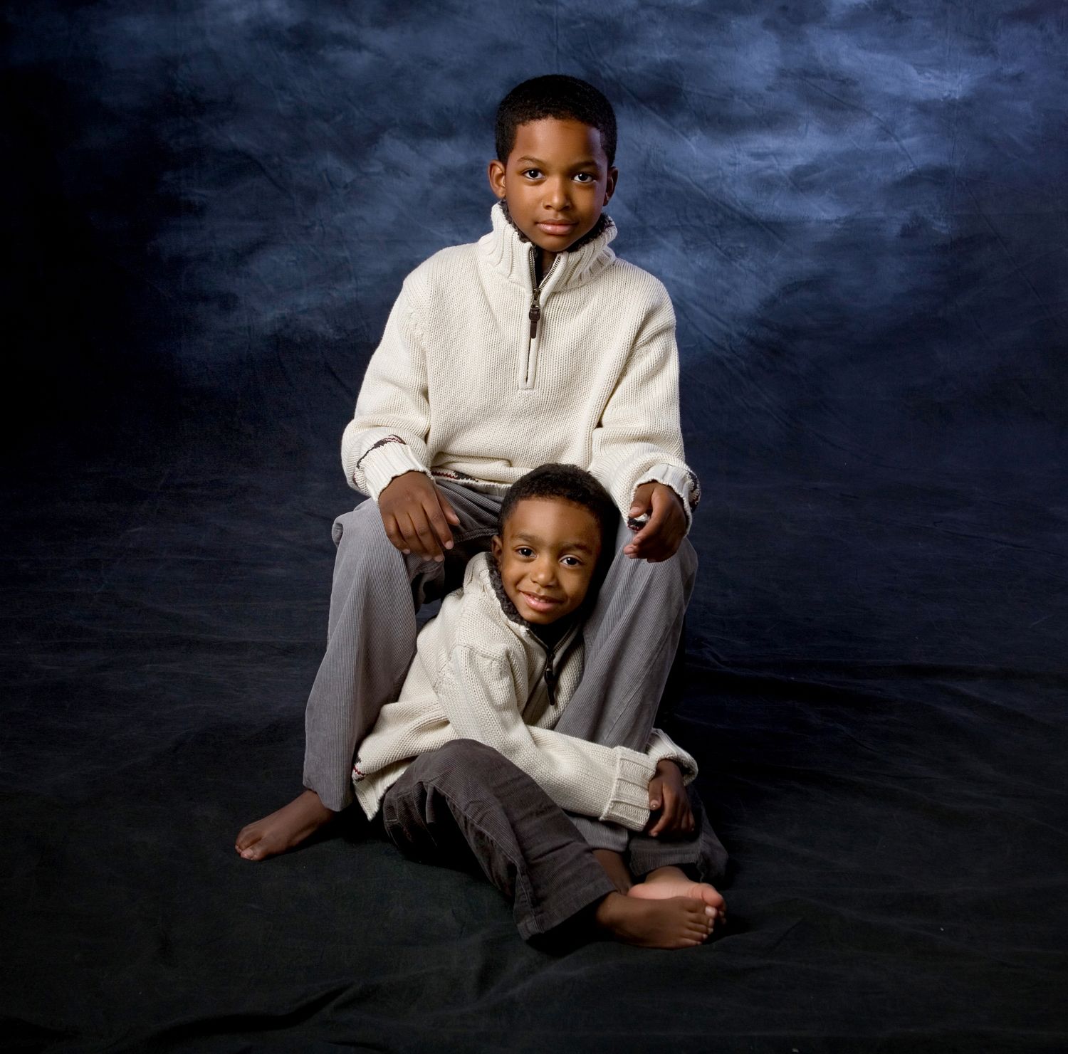 Two young boys pose for a studio portrait, wearing matching white fleece pullovers and gray pants.