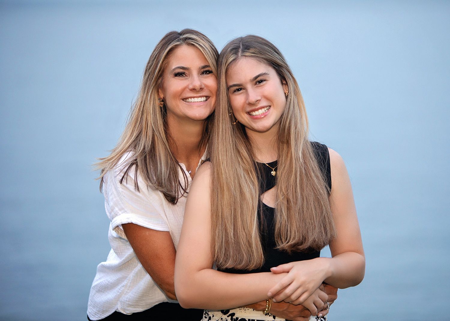 A mother and her high school senior daughter pose together outdoors near water in a warm, friendly portrait.