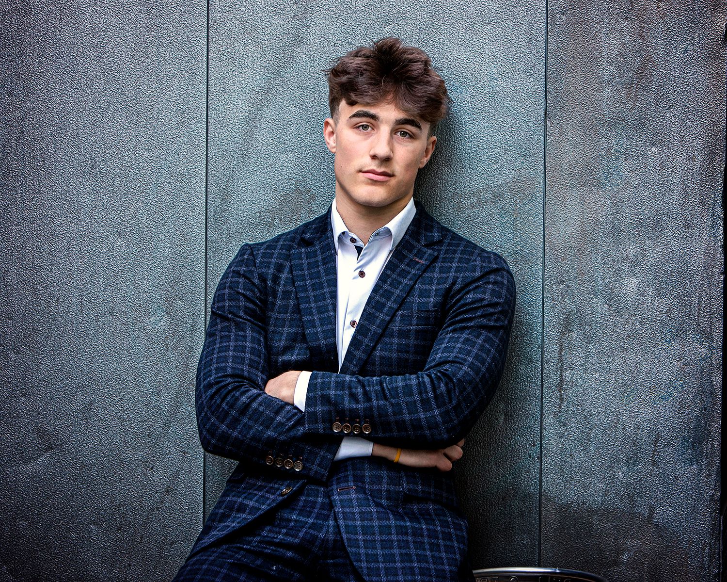 : Editorial guy's senior portrait in Rochester, MI by Jocelyn M. Photography—young man in a blue plaid suit by a gray wall.