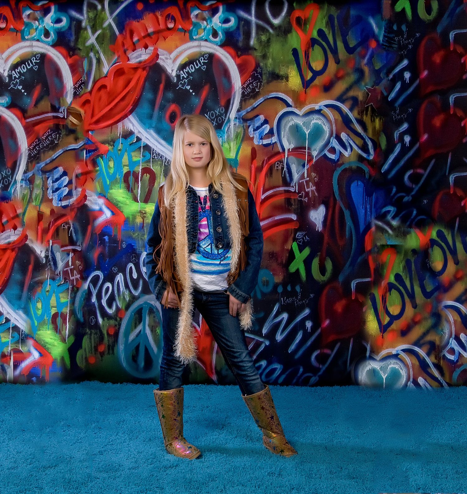 Young girl posing confidently in front of colorful graffiti wall with hearts and peace signs.