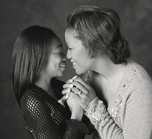 Black and white portrait of mother and daughter smiling face to face, holding hands tenderly.