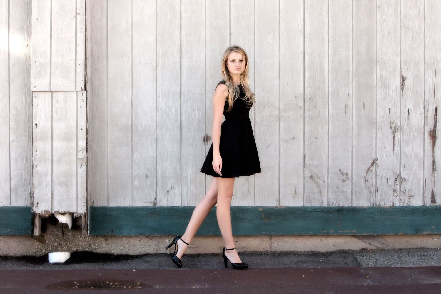 Urban senior girls portrait in Rochester, MI by Jocelyn M. Photography—blonde teen in black dress by weathered white door.