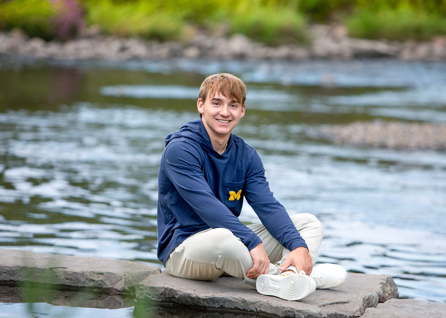 Senior guy in Michigan hoodie sitting on rocks  in Rochester, MI by Jocelyn M. Artistic Photography