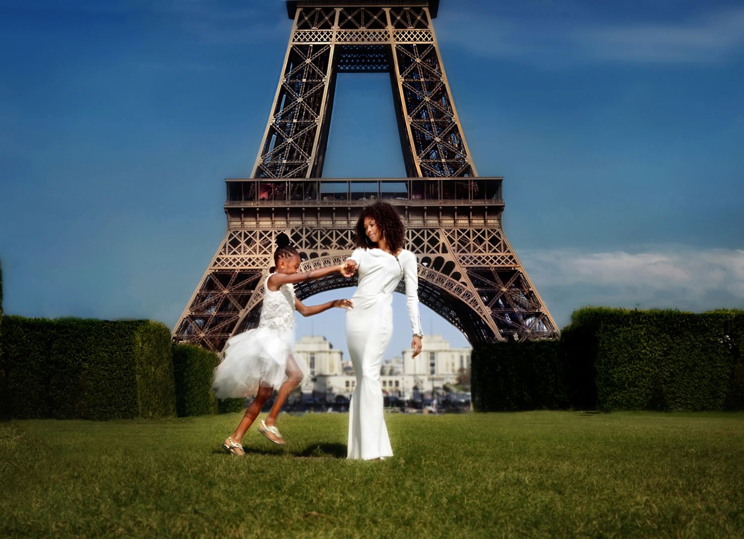Woman in white dress dancing with young girl in tutu in front of the Eiffel Tower in Paris, France.