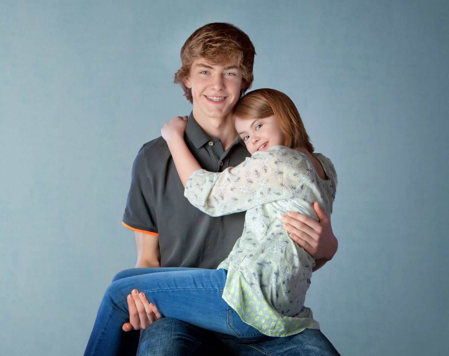 Teen boy smiling and hugging a young girl in a studio portrait photo.