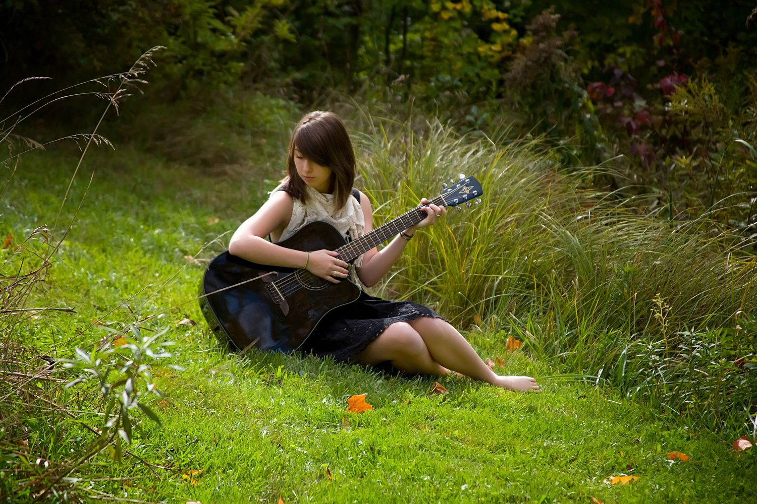 Senior girl playing acoustic guitar while sitting on green grass in a lush garden setting,by Jocelyn M. Photography in Rochester, MI