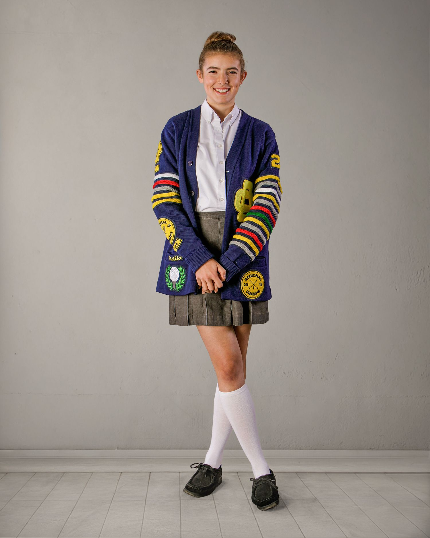 Smiling student in navy varsity cardigan and school uniform posing against a gray background.