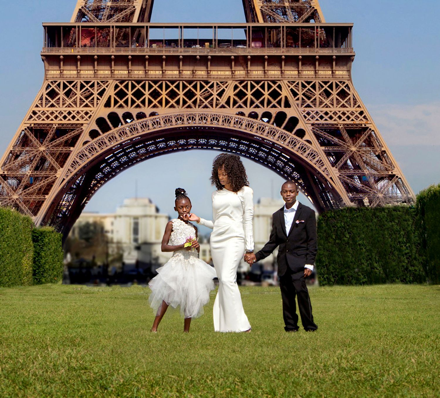 Family in elegant attire poses before the Eiffel Tower in Paris, France, on a sunny day.