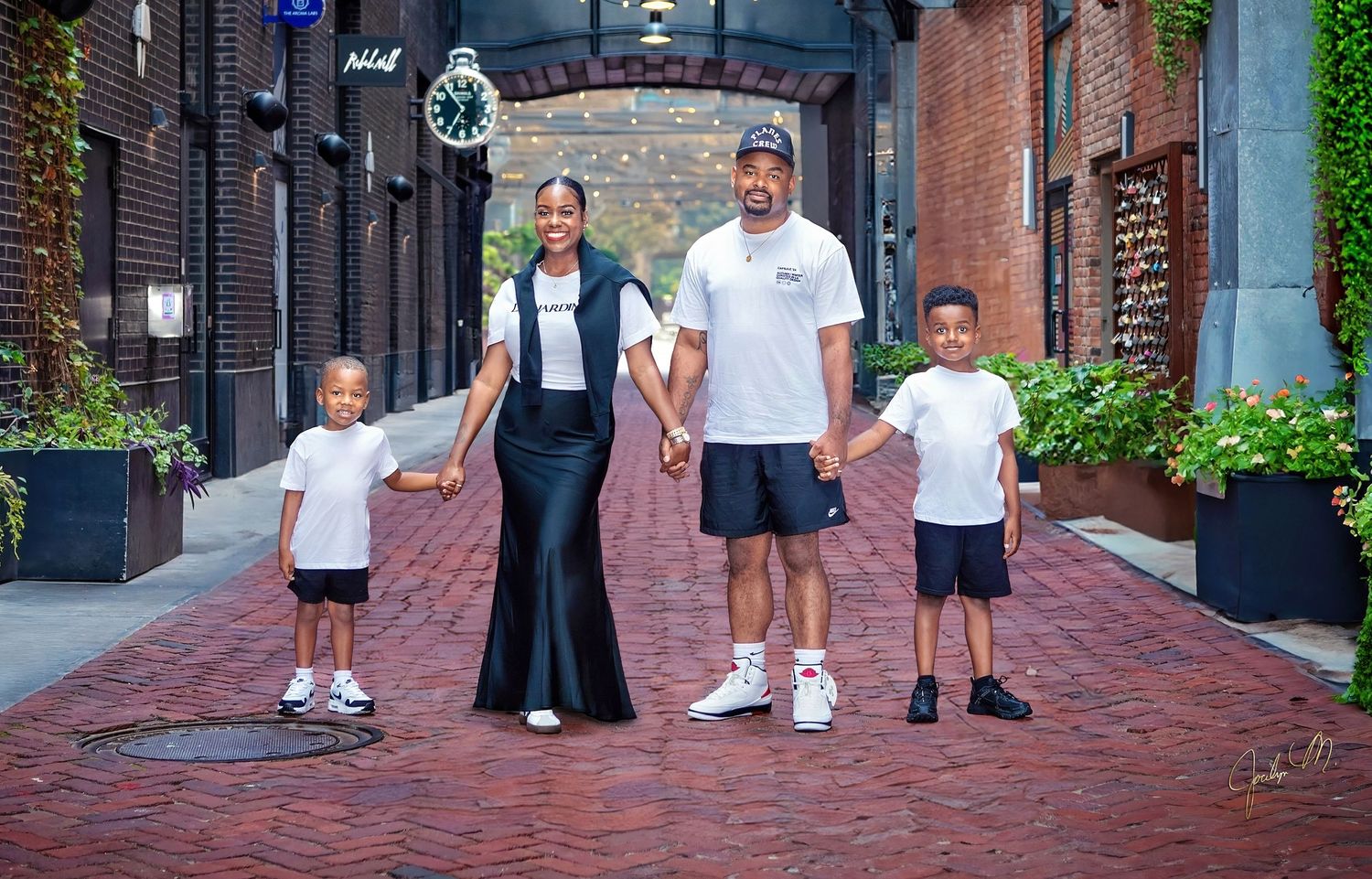 Family of four holding hands and walking on a brick street outdoors.