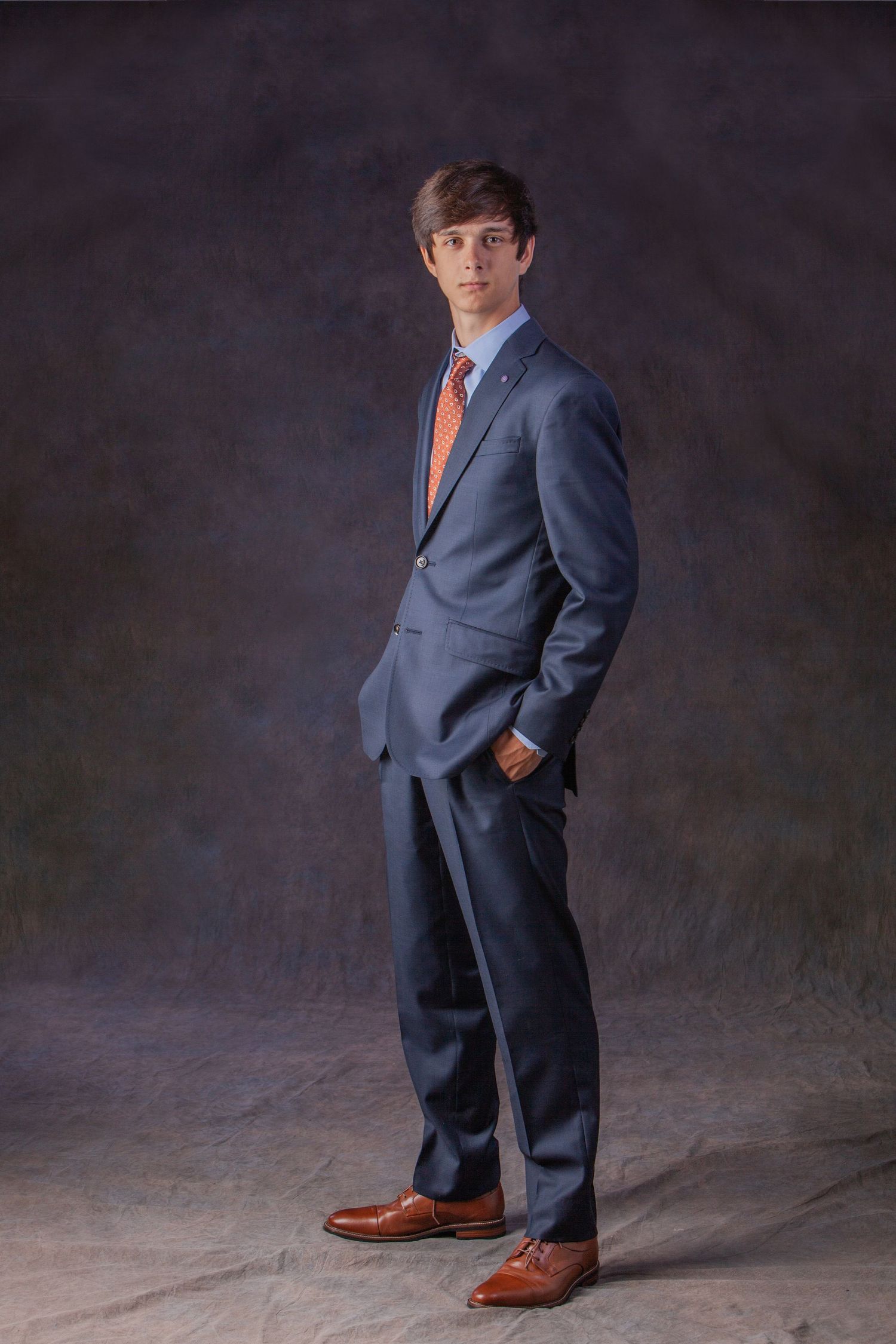 Guys senior portrait session in Rochester, MI by Jocelyn M. Photography—young man in navy blue suit on gray backdrop.