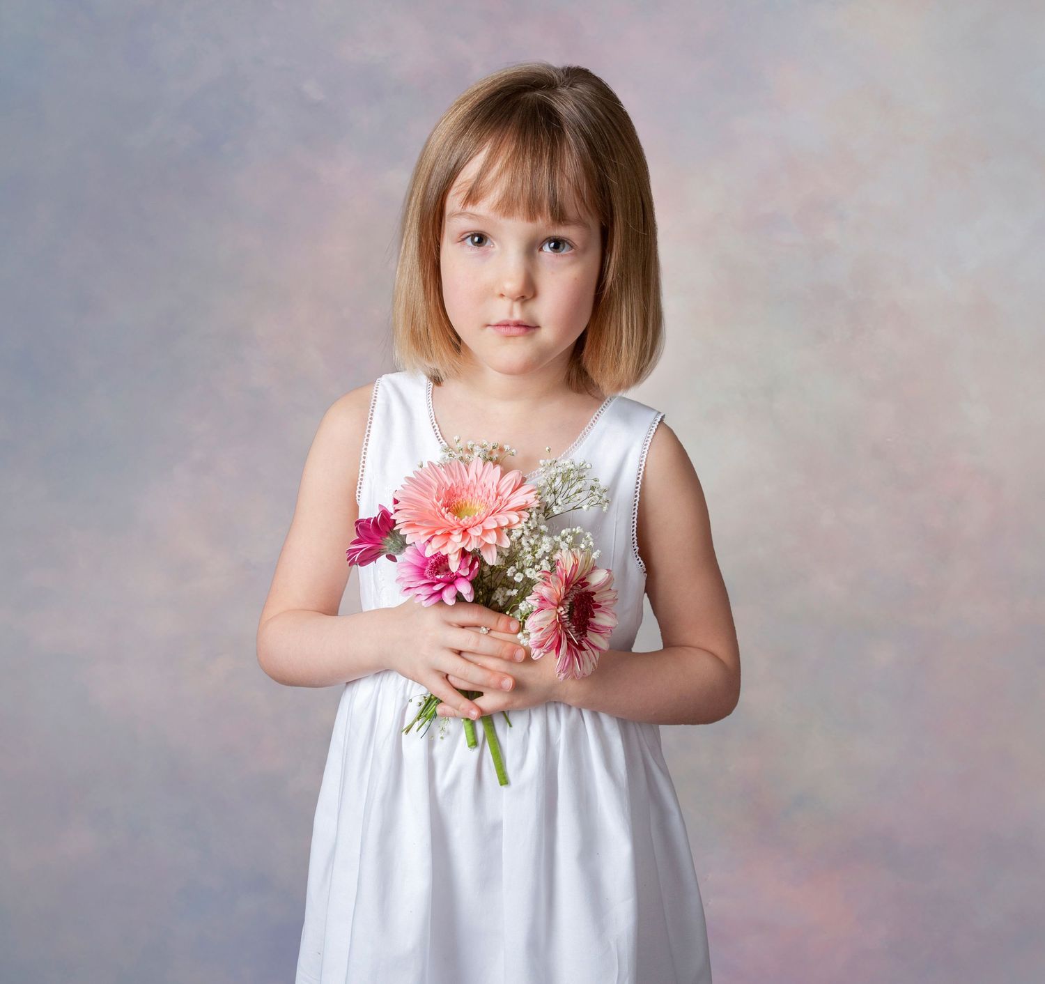 Young girl in white dress holding pink gerbera daisy bouquet in studio portrait photography.