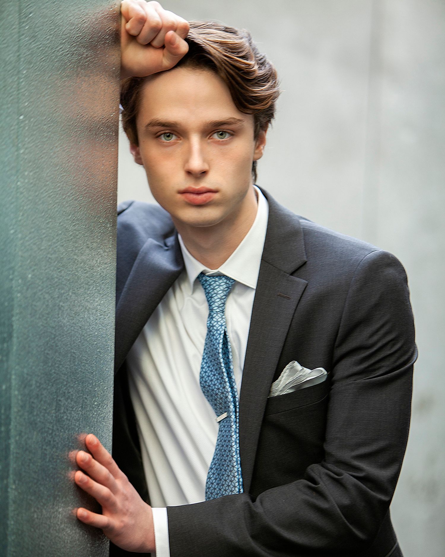 Editorial guys senior portrait in Rochester, MI by Jocelyn M. Photography—young man in a dark suit leaning on a wall.