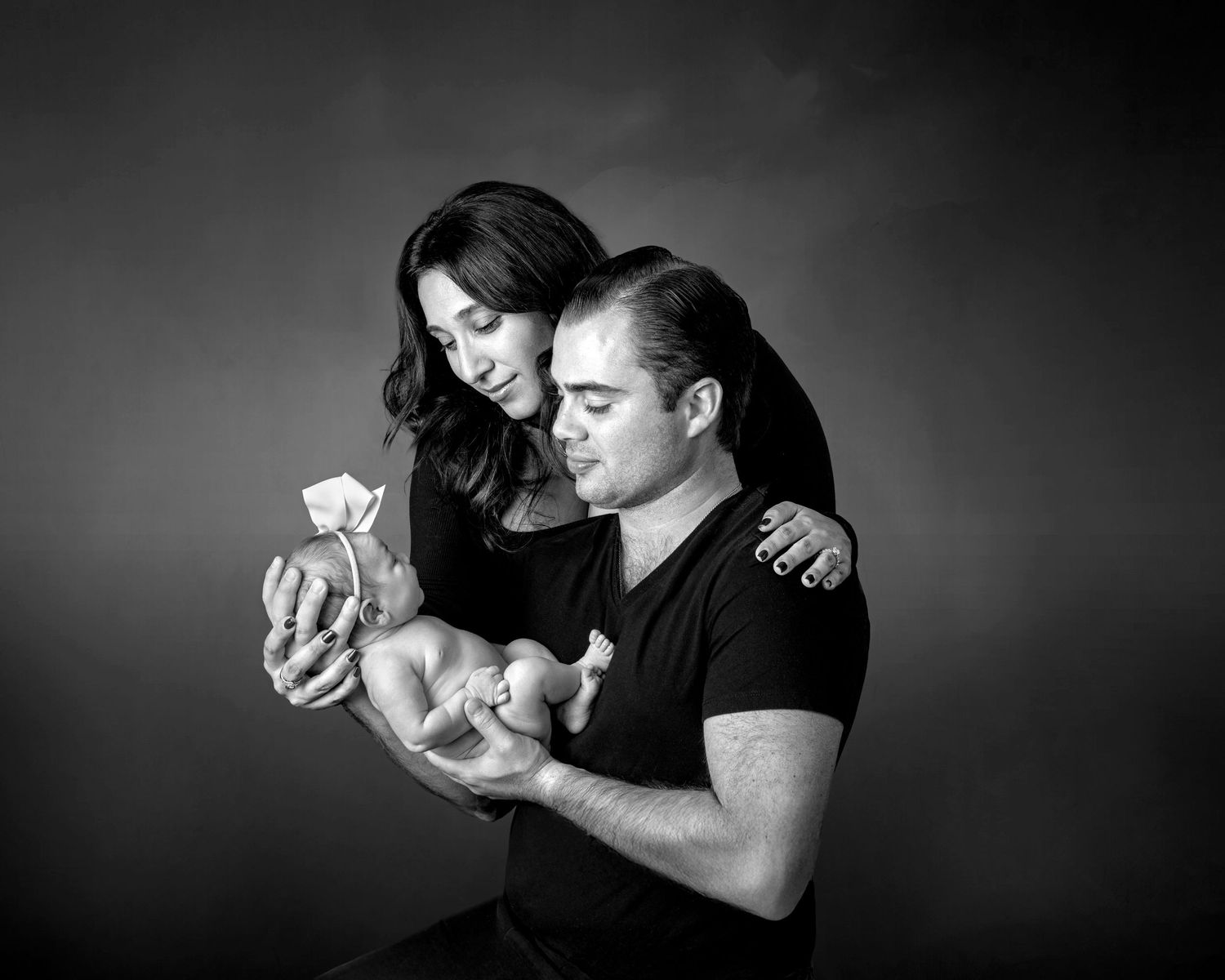 Black and white photo of parents tenderly holding their newborn baby together in a studio portrait.