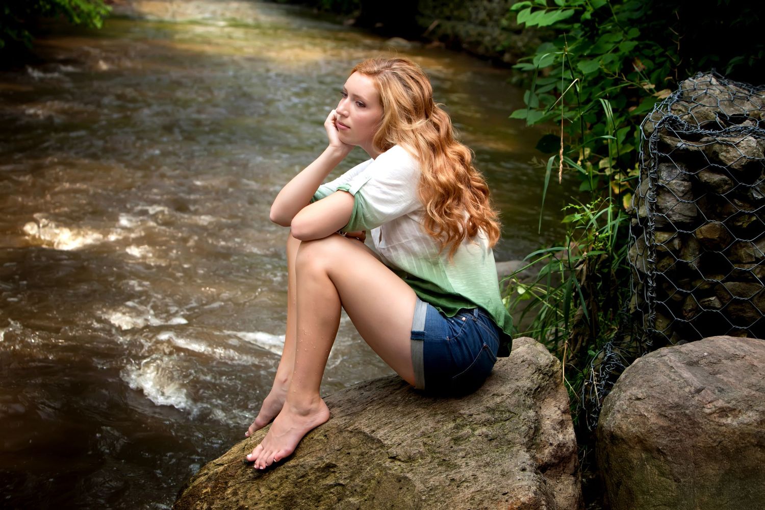 Signature senior session in Rochester, MI by Jocelyn M. Photography—young woman with red hair sitting by a peaceful stream.