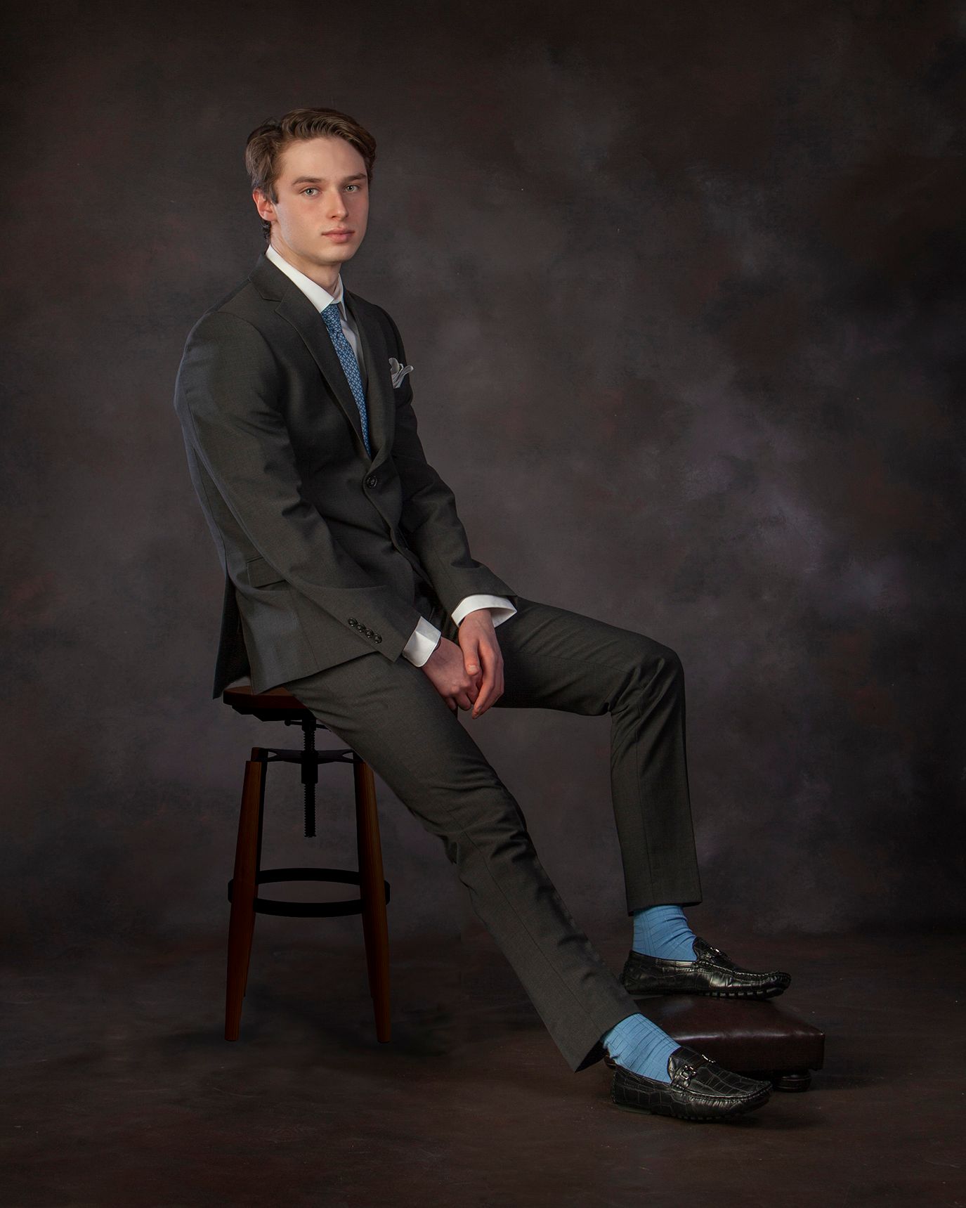 Studio senior portrait in Rochester, MI by Jocelyn M. Photography—young man posing on a stool in a classic dark suit.