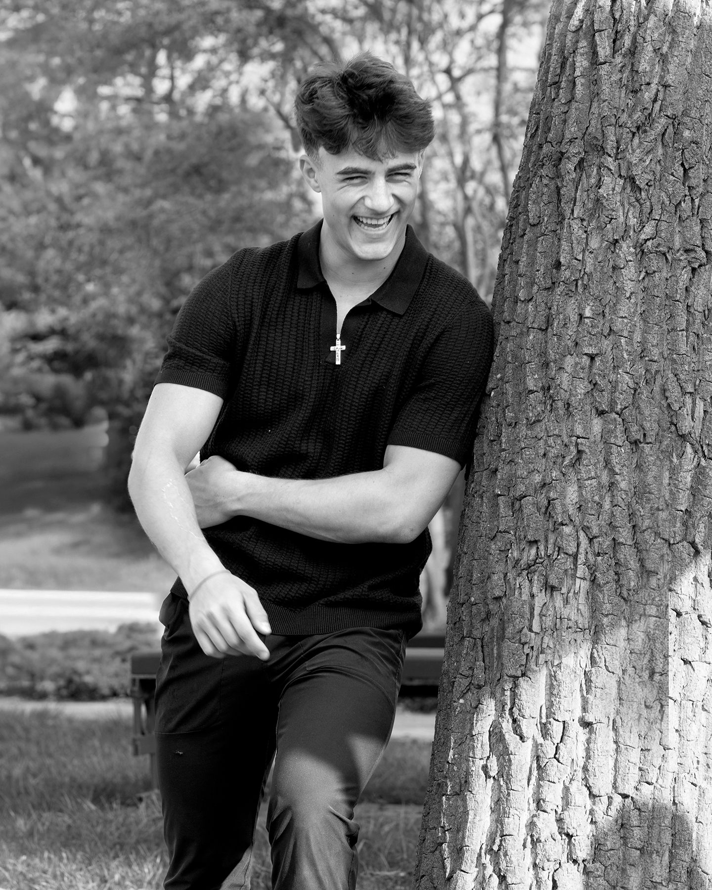 Black and white guy's senior portrait in Rochester, MI by Jocelyn M. Photography—young man laughing by a park tree.