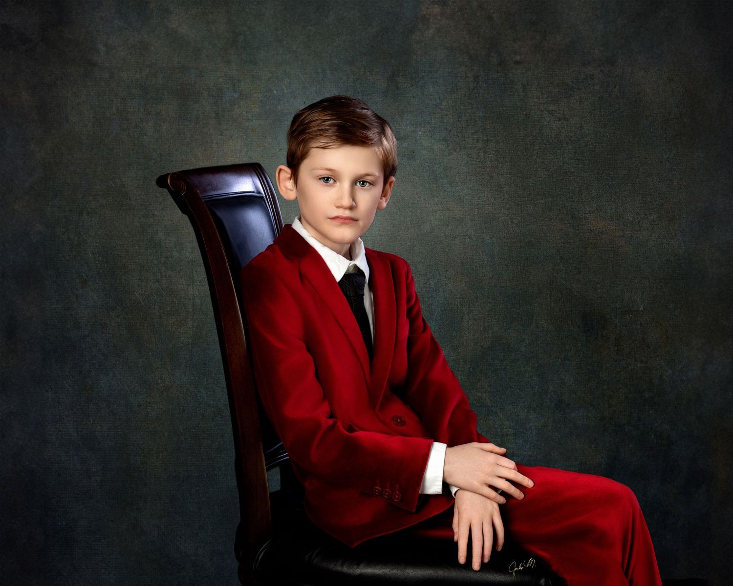 Fine art children's studio portrait in Rochester, MI by Jocelyn M. Photography—young boy in a red velvet suit in dark chair.