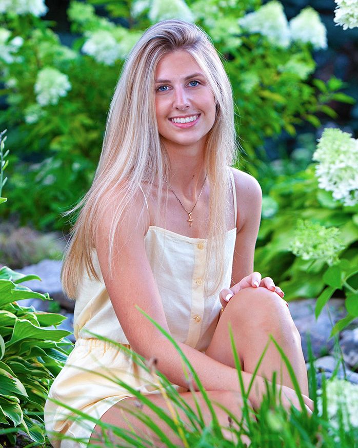 Smiling senior girl  among lush green plants and white hydrangeas outdoors, by Jocelyn M. Photography in Rochester, MI