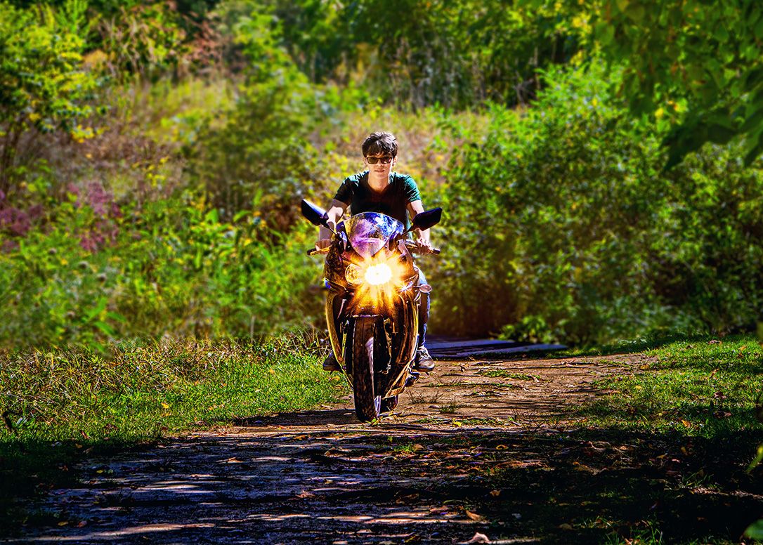 Person riding a motorcycle on a scenic dirt path surrounded by lush green foliage.