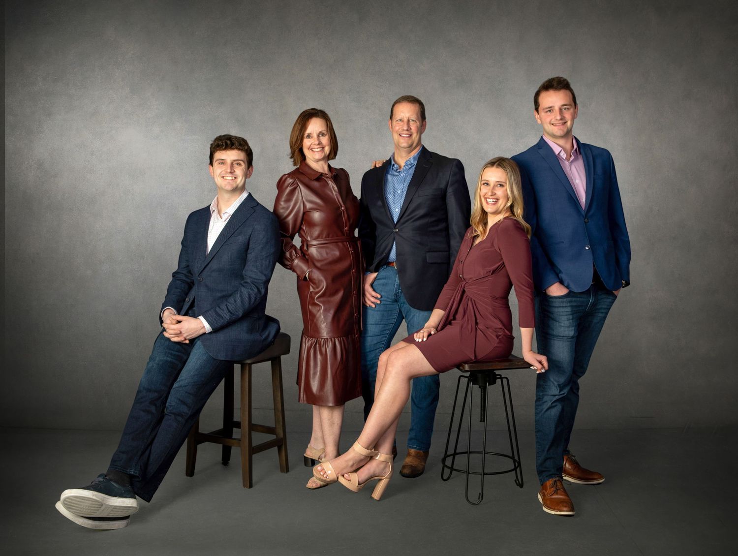 Five professionally dressed adults posing together for a formal group portrait against a gray studio background.