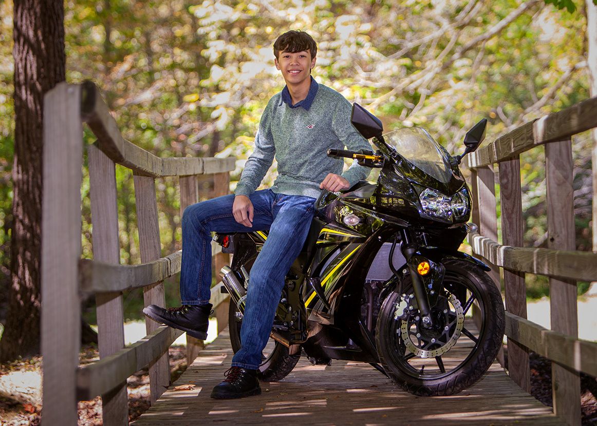Young man in blue sweater posing on black and yellow sport motorcycle on wooden bridge.