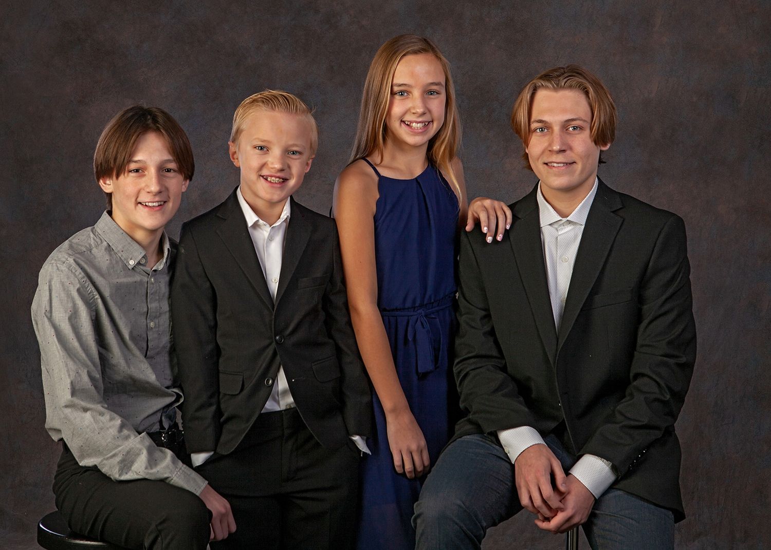 Four children in formal attire pose together for a professional studio portrait photo.
