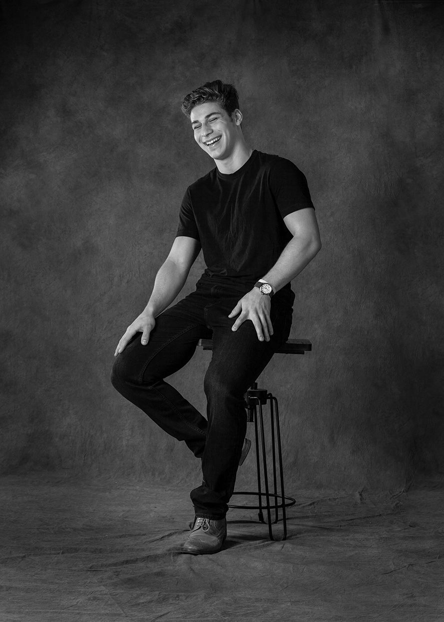 Black and white senior portrait in Rochester, MI by Jocelyn M. Photography—young man sitting on a stool laughing.