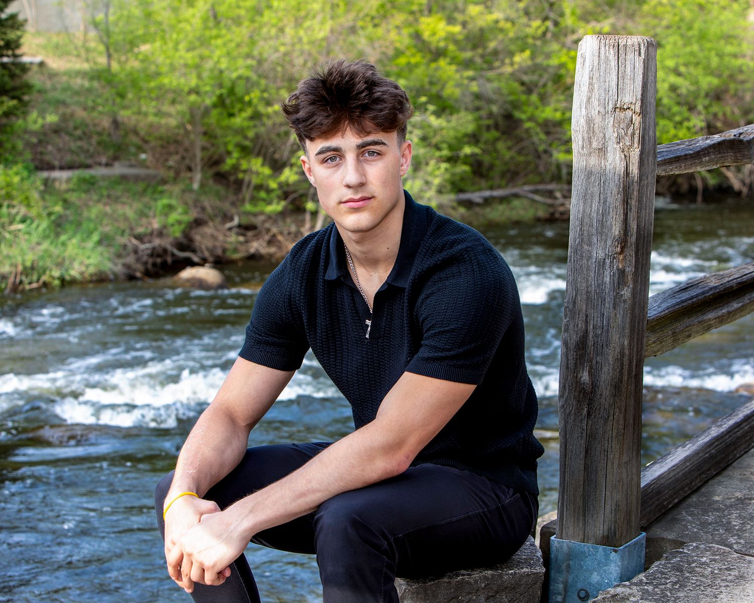 Senior portrait for guys in Rochester, MI by Jocelyn M. Photography—young man sitting on a stone ledge by a creek.