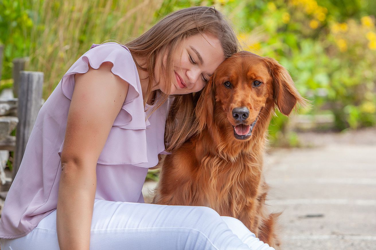 Smiling young woman in pink top bonding with a golden retriever dog outdoors.
