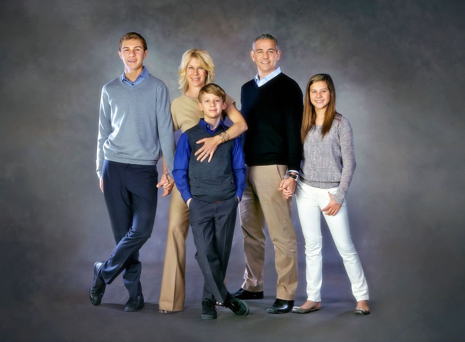 Family of five posing for a professional portrait against a gray studio background, dressed in casual elegant attire.