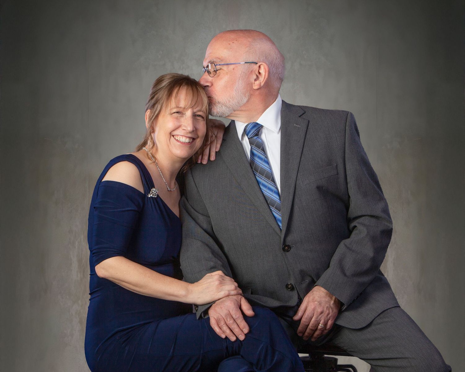 Older couple sharing a tender kiss during a professional studio portrait session, woman smiling in blue dress.
