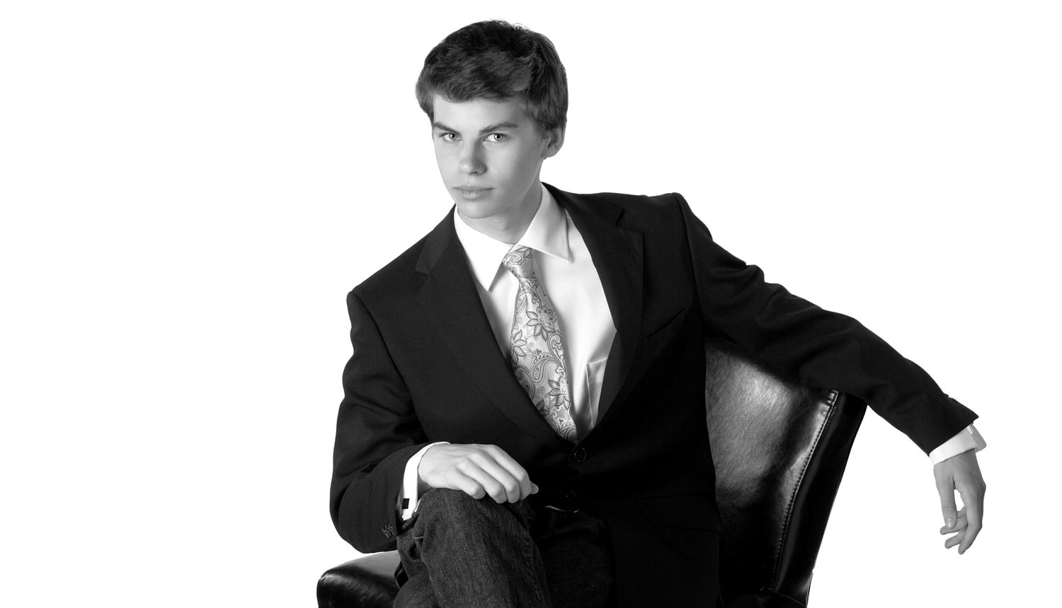 Young man in black suit and tie in Rochester, MI by Jocelyn M. Artistic Photography in leather chair, black and white portrait