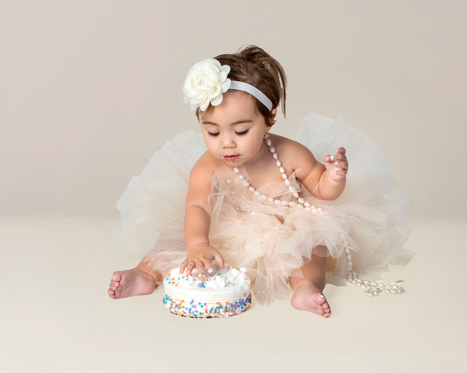 First birthday cake smash portrait in Rochester, MI by Jocelyn M. Photography—baby girl in tutu with birthday cake.