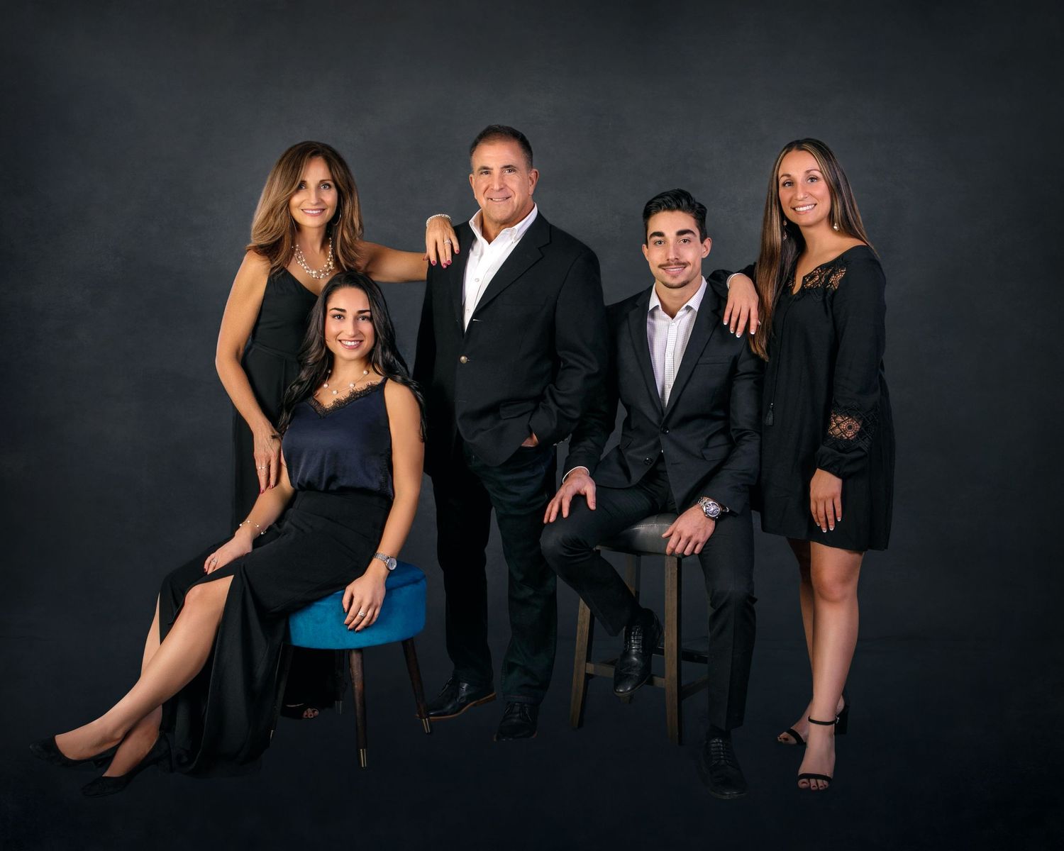 Professional family portrait of five elegantly dressed adults posing together against a dark studio background.