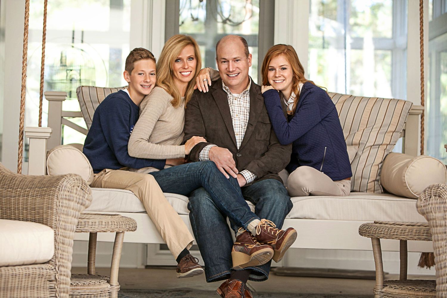 Happy family of four smiling together on a cozy wicker couch in a bright, elegant living room.