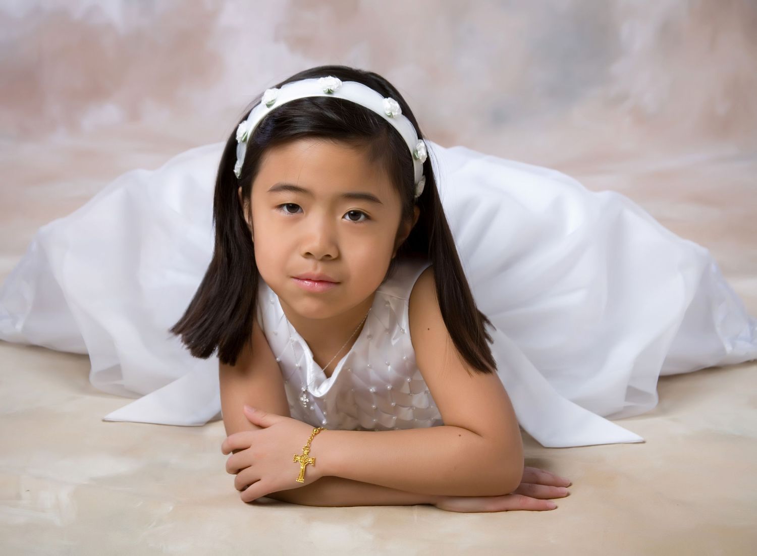 Young Asian girl in white First Communion dress lying on studio floor.