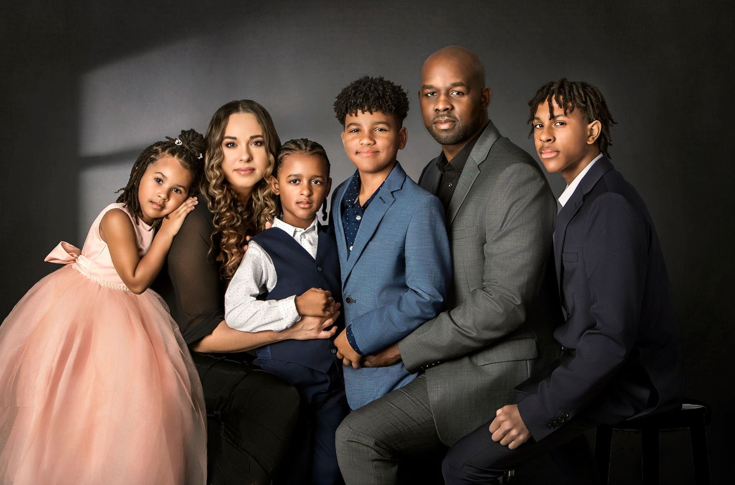 A family of six poses together for a professional portrait against a dark background in formal attire.