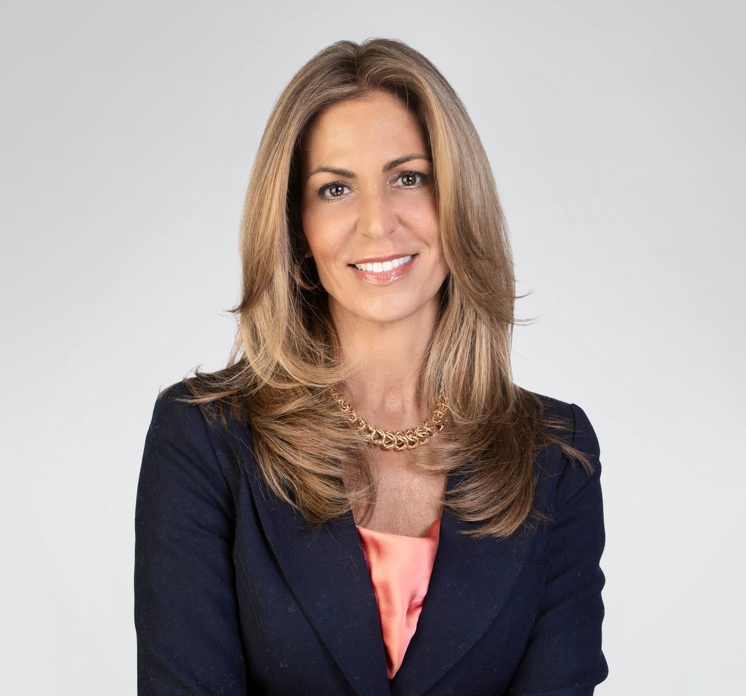 Professional woman with long brown hair in navy blazer smiling for corporate headshot.