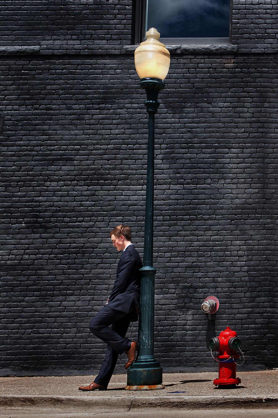 Urban senior portrait in Rochester, MI by Jocelyn M. Photography—young man leaning against a green street lamppost.