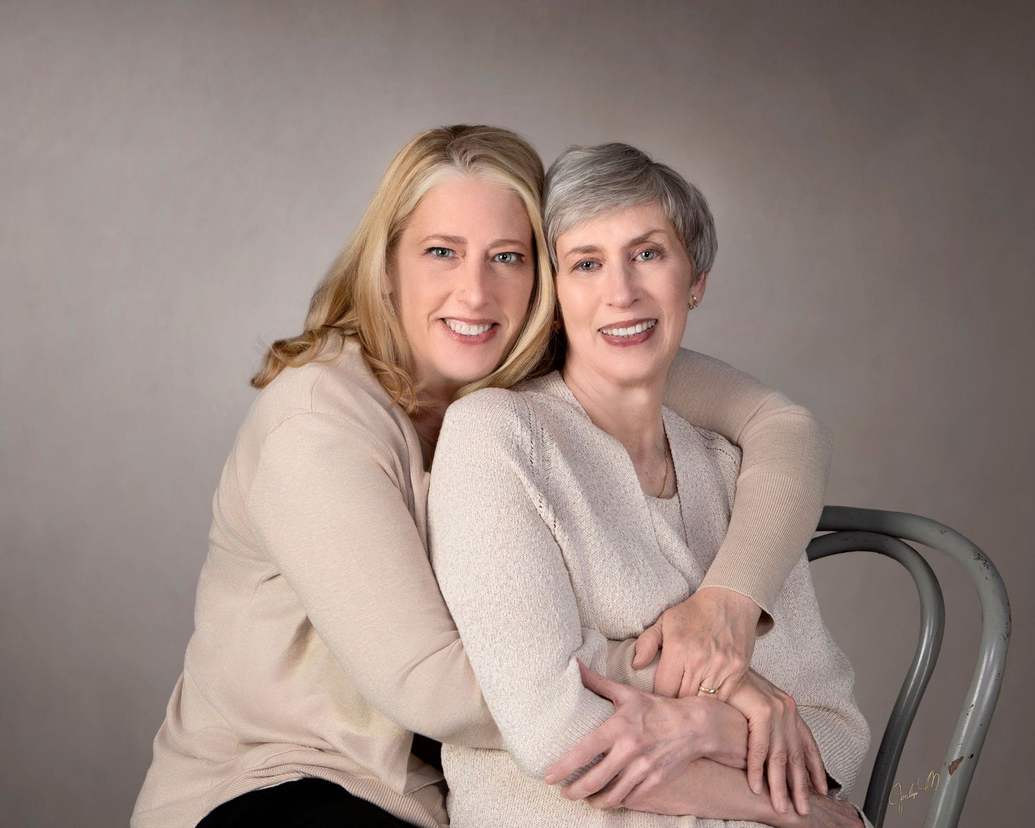 Two women smile warmly together in coordinating beige outfits for a professional studio portrait.