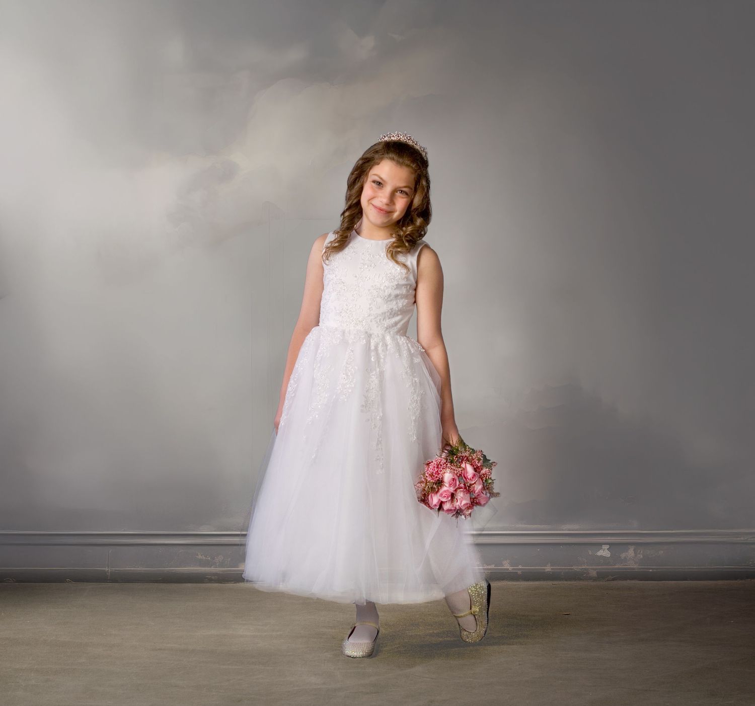Young girl in white tulle flower girl dress holding pink bouquet in studio portrait.