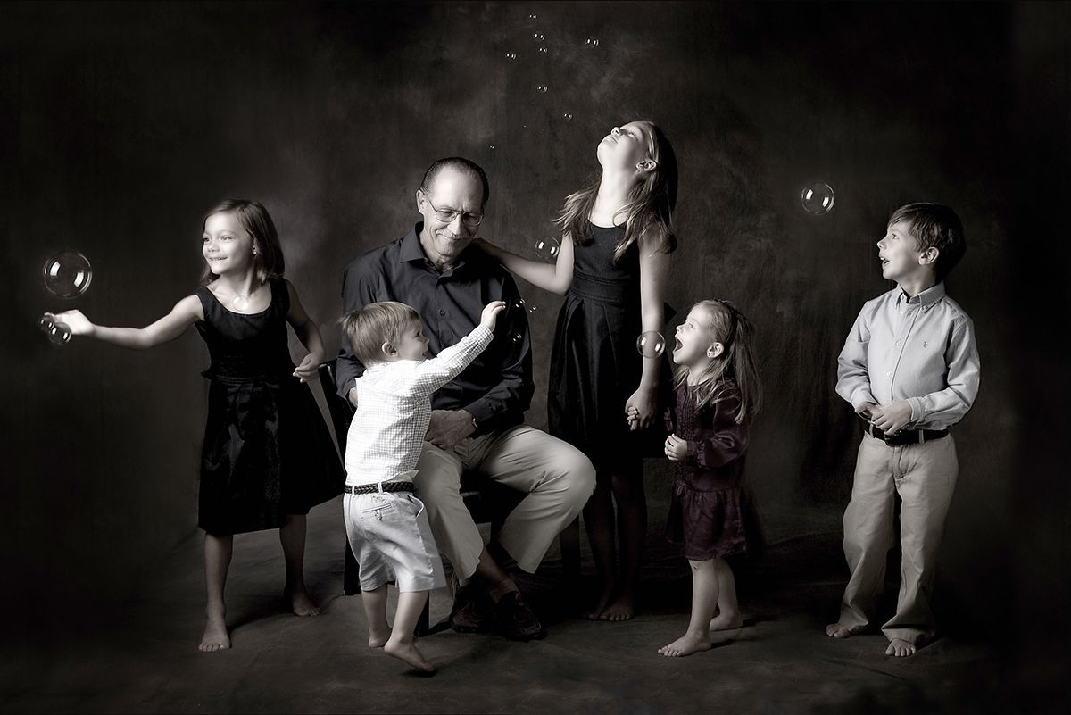 Black and white family portrait with parents and four children playing with bubbles in a studio setting.
