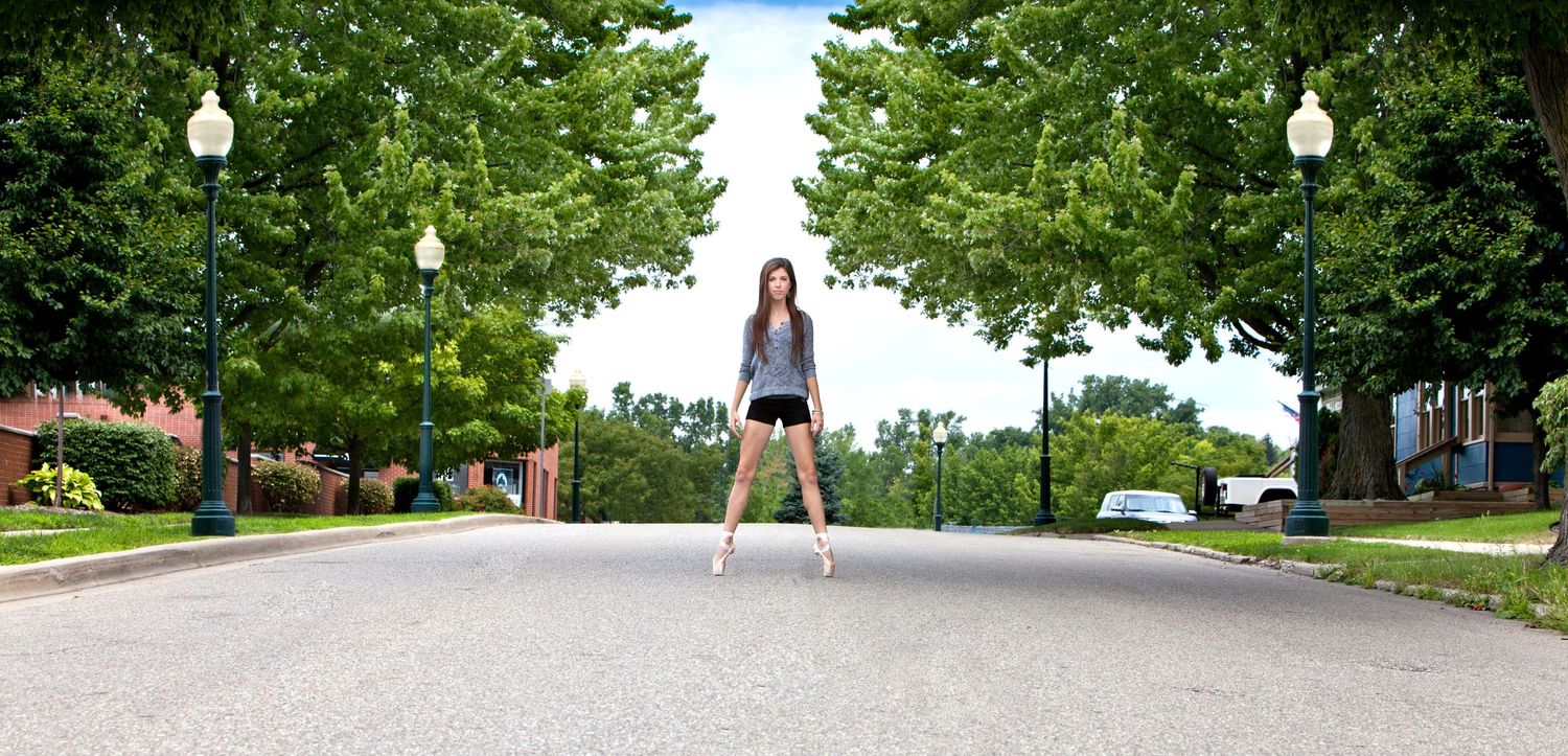 Senior girl standing confidently on a tree-lined road in shorts and heels on a sunny day, by Jocelyn M. Photography in Rochester, MI.