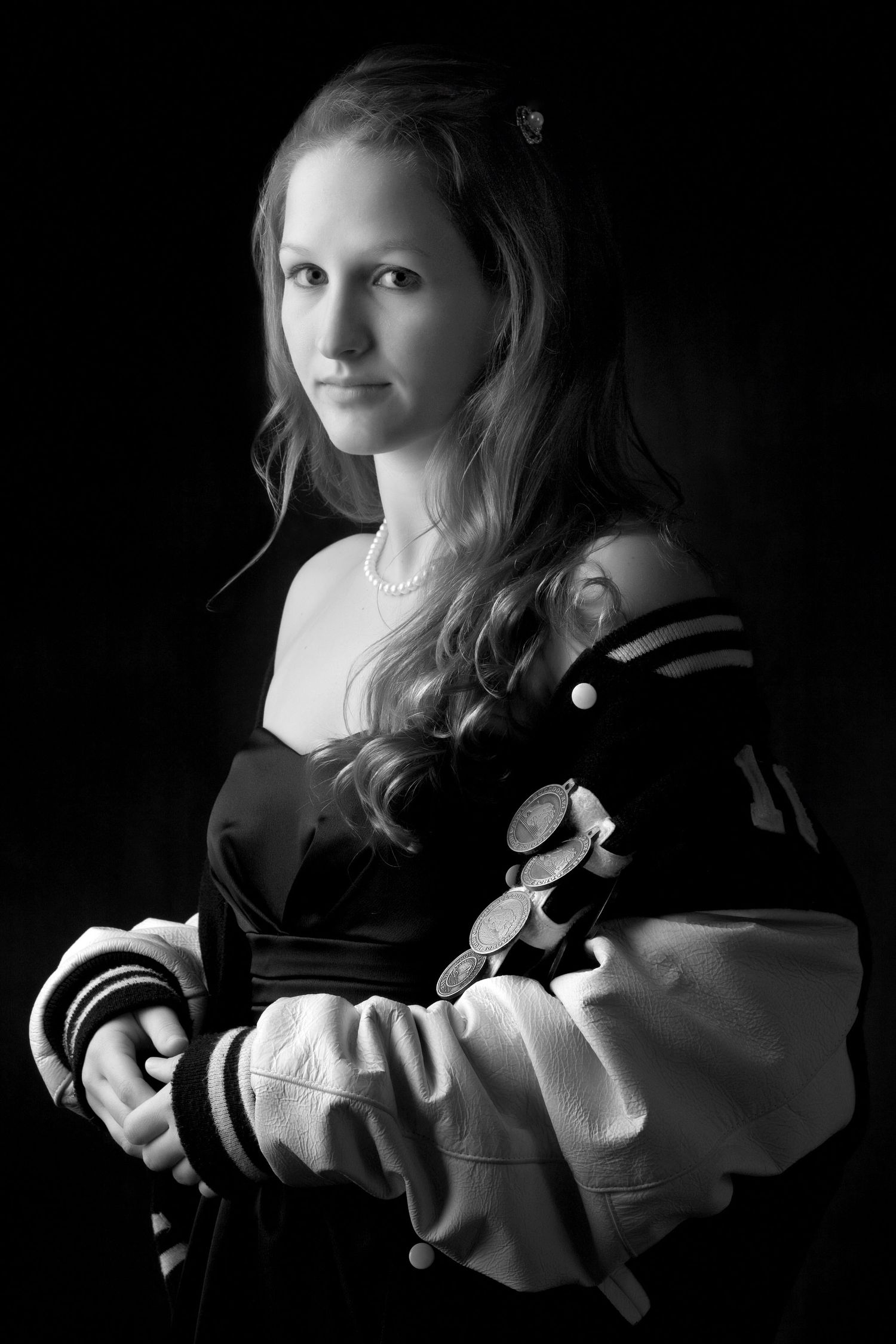 Black and white portrait of a young woman in a varsity jacket, posing against a dark background.